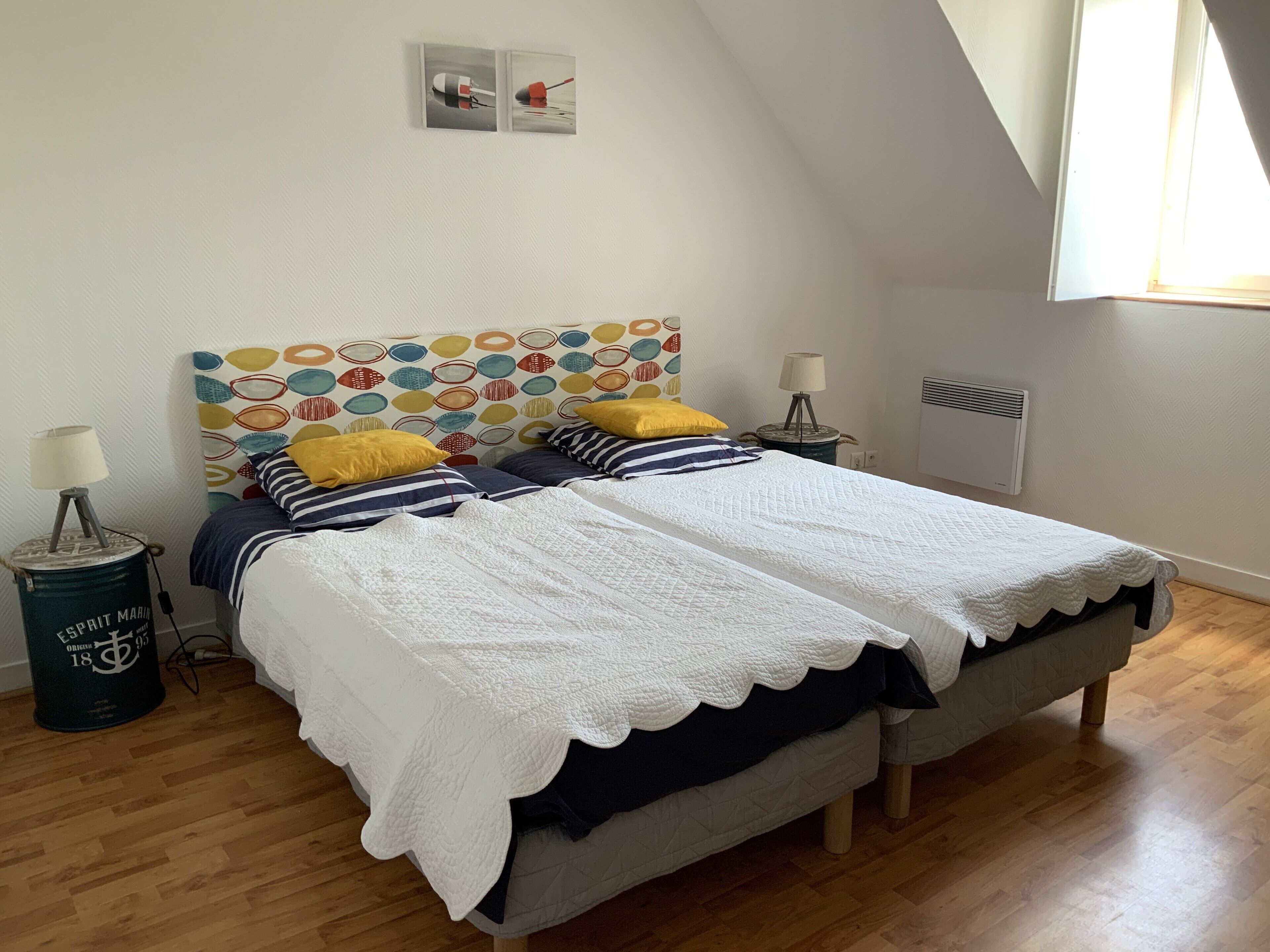 Une chambre à coucher avec un lit, deux tables de chevet, une lampe, un radiateur et une fenêtre.