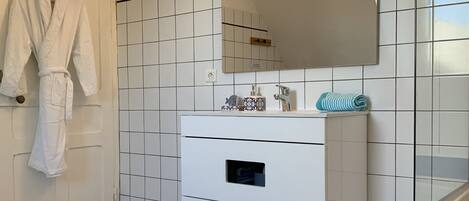 A bathroom with white tiled walls, a white sink with a mirror, and a wooden floor.