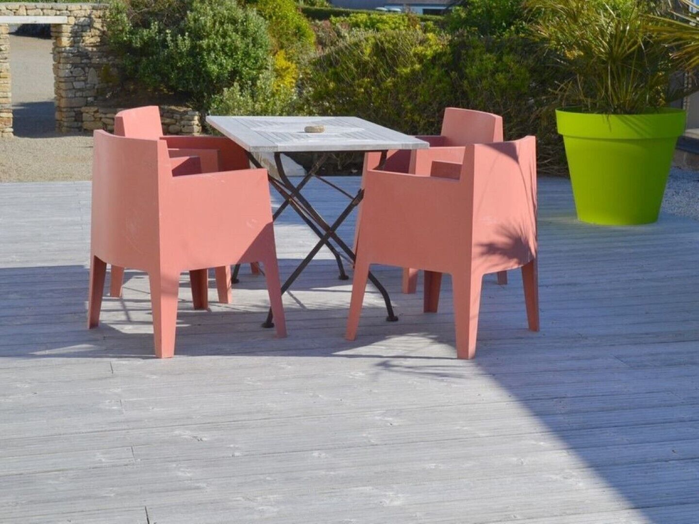 A wooden deck with a table and four pink chairs.