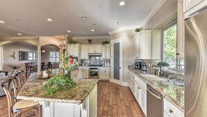 Una cocina amplia con encimeras de granito, armarios blancos y una isla central con un jarrón de flores.