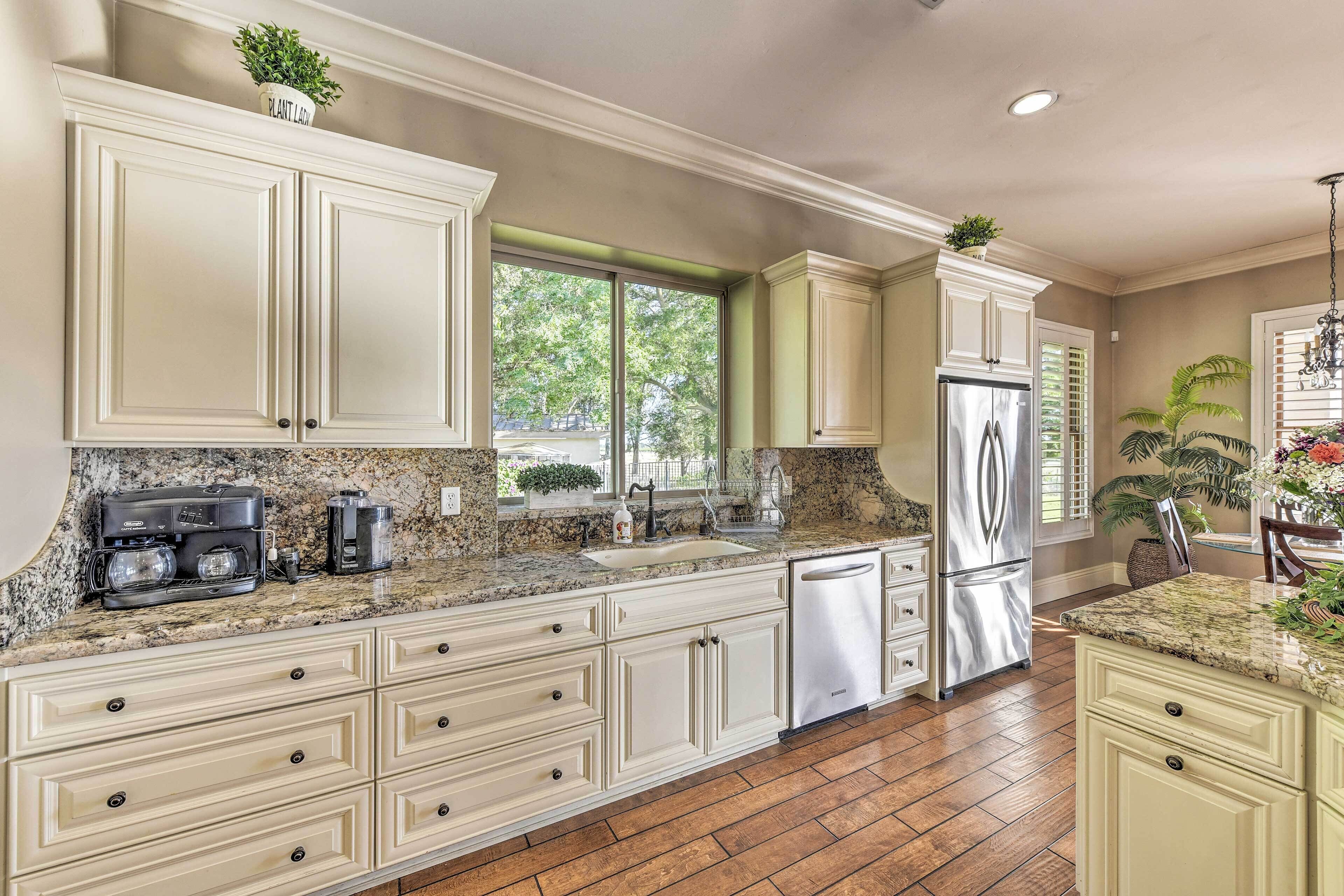 A kitchen with white cabinets, a stainless steel refrigerator, a coffee maker, and a window with a view of trees.