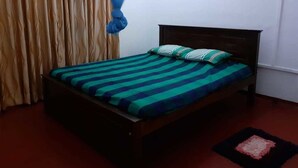 A single bed with a striped bedspread and two pillows, a wooden headboard, a dark-colored rug, and a curtain with a blue canopy.
