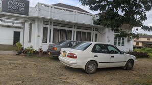 A building with a sign reading "UMAYA REST INN". There are two cars parked in front, and the building has large windows and a tiled roof.