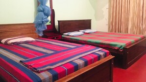 A room with two beds, each with a striped bedspread, a wooden headboard, and a nightstand.