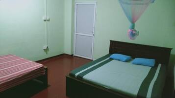 A room with two beds, one with a striped bedspread and the other with a solid bedspread and two pillows.