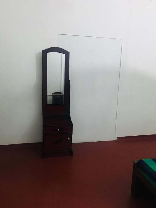 Quarto com cômoda de madeira escura em parede branca, tapete vermelho e um banco listrado em verde e azul.