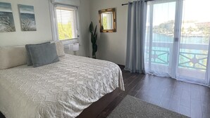 Una camera da letto con un letto grande, un ventilatore a soffitto, una finestra con tende e vista su un corpo d'acqua.