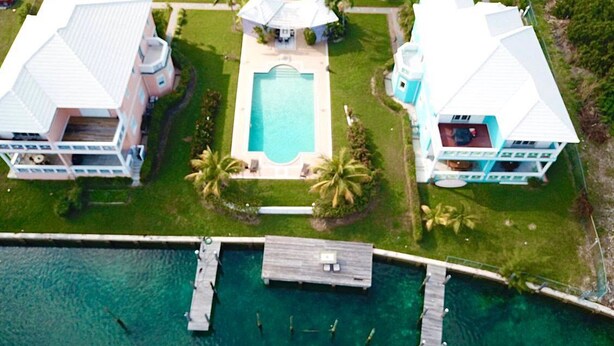 Vista aerea di un resort con piscina, diversi edifici e un molo che si protende su acque turchesi.