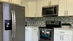 Una cucina moderna con mobili bianchi, un frigorifero in acciaio inossidabile, un forno a microonde e un forno.