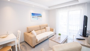 A modern living room with a beige sofa, a white table, a TV, and a balcony with a view. - Cubo's Apartamento Tivoli B3 / free wifi / air conditioning (Benalmádena)