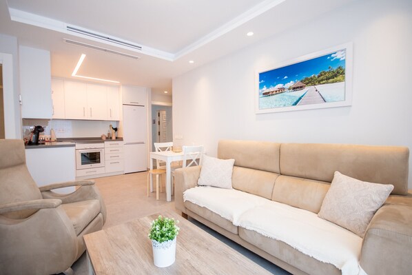 A modern living room with a beige sofa, a coffee table with a plant, and a dining area with a white table and chairs. - Cubo's Apartamento Tivoli B3 / free wifi / air conditioning (Benalmádena)