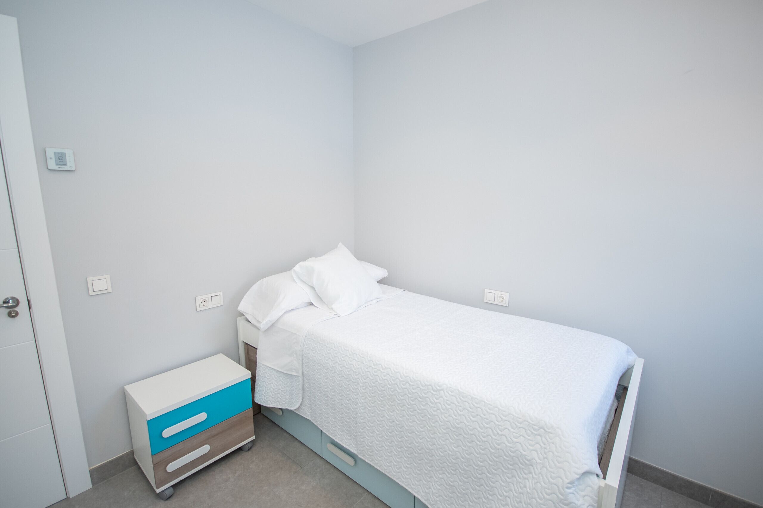 Une petite chambre à coucher, bien rangée, avec un lit simple, une table de chevet et un meuble de rangement.