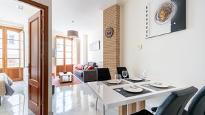 Un espace repas moderne avec une table blanche dressée pour quatre personnes, un mur en briques apparentes et une grande peinture abstraite au-dessus de la table.