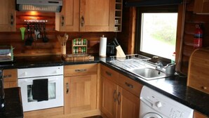 A compact kitchen with wooden cabinets, a built-in oven, a dishwasher, and a window providing natural light. - Braeside by Interhome (Invergarry)
