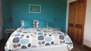 Un dormitorio con una pared verde azulado, una cama con edredón estampado, dos mesitas de noche con lámparas y una puerta de madera.