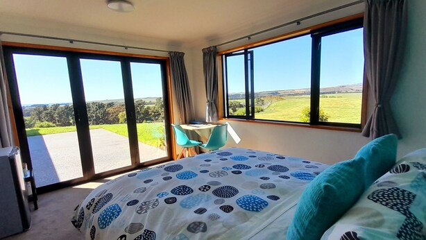 Un dormitorio con una cama grande, un escritorio y vistas a un paisaje verde a través de las ventanas.