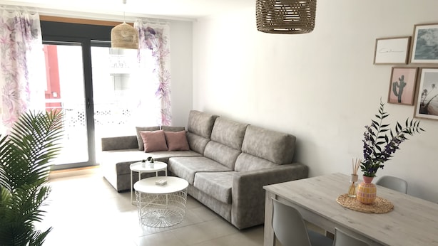 Ein modernes Wohnzimmer mit einem grauen Sofa, einem kleinen runden Tisch und einem Essbereich mit einem Holztisch und Stühlen.