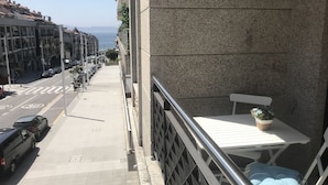Ein Balkon mit weißem Tisch und blauer Auflage, mit Blick auf eine Straße mit parkenden Autos und Gebäuden.