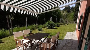 Un patio al aire libre con un toldo a rayas, piso de baldosas de piedra y una mesa de madera con sillas.