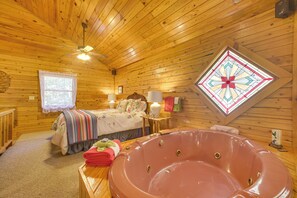 Une chambre de style cabane en bois, avec un lit, une grande baignoire, un ventilateur de plafond et une fenêtre à vitraux.