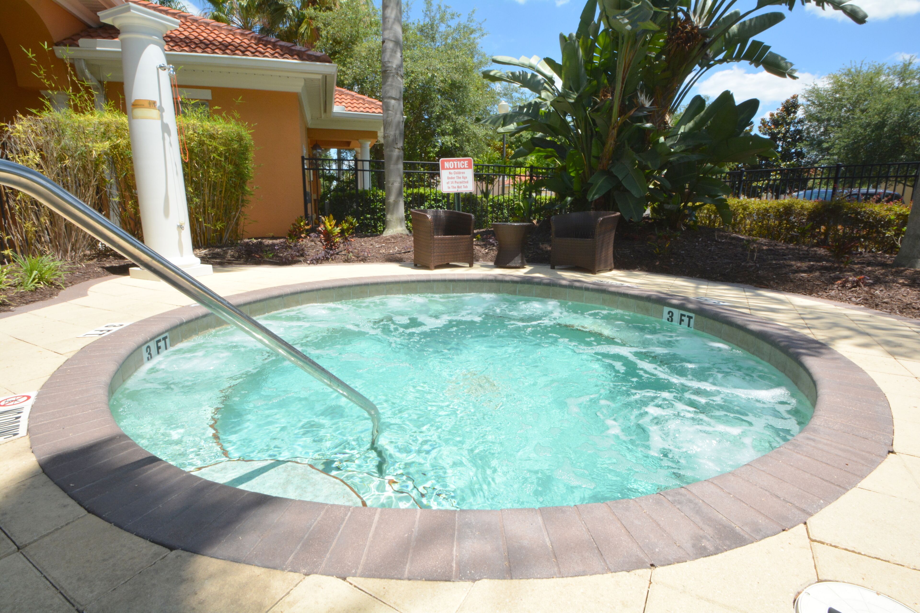 A hot tub with a 3 FT depth label, surrounded by a brick border and a poolside area with wicker chairs and a notice sign.