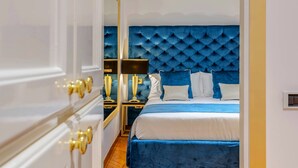 A bedroom with a wooden floor, a blue upholstered headboard, and a white bedspread. - SPANISH STEPS Extra Luxury Apartment (Roma)