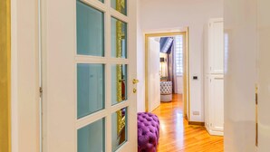 A hallway with a white door, a purple tufted bench, and a glimpse of a room with a window and curtains. - SPANISH STEPS Extra Luxury Apartment (Roma)