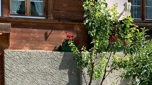 A patio with two metal chairs and a small table, a stone wall, and a tree with red flowers. - Apartment on the farm (Gadmen)