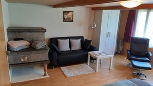 A living room with a black sofa, a white coffee table, a stone fireplace, and a black armchair. - Apartment on the farm (Gadmen)