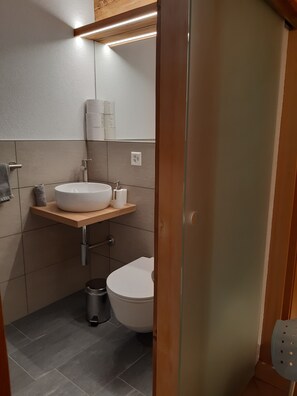 A modern bathroom with a white sink, toilet, and a small trash bin.
