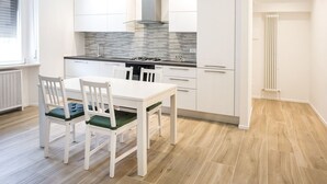 Une cuisine moderne avec des meubles blancs, une cuisinière à gaz et une fenêtre équipée de stores.