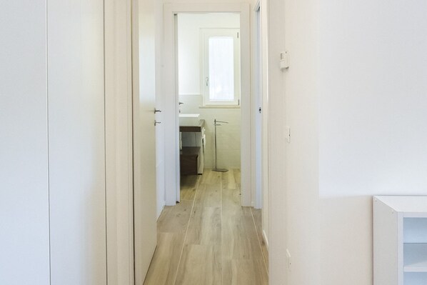 Un estrecho pasillo con suelo de madera que conduce a un baño con ventana.