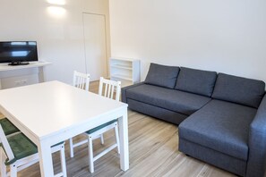 Un salon avec une table blanche, un canapé gris et un téléviseur posé sur un meuble.