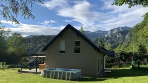 Una casita con piscina en un jardín cubierto de césped, rodeada de montañas.