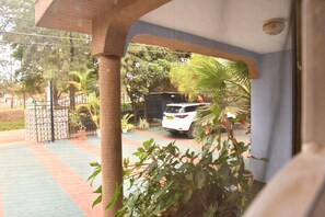 A covered outdoor area with a paved walkway, potted plants, and a parked white car. - Mzunguu Safari Lodge (Arusha)