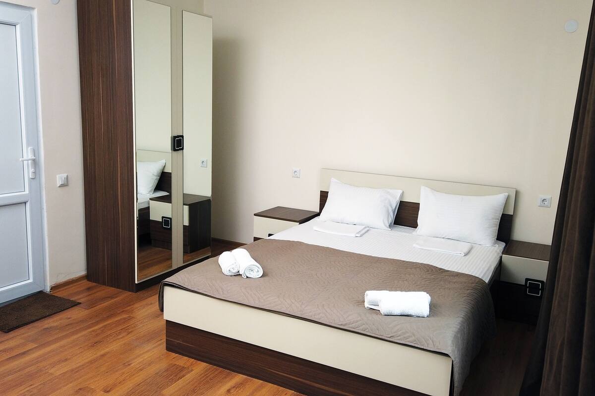 A neatly arranged hotel room with a large bed, a bedside table, a nightstand, a mirror, and a door.