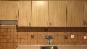 A kitchen with wooden cabinets, a stainless steel sink, and a hanging light fixture. - Taygetos (Sparta)