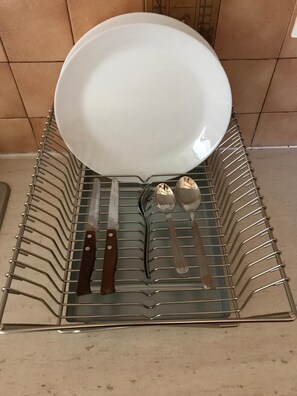 A metal dish rack with a white plate, two knives, and two spoons. - Taygetos (Sparta)