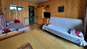 Ein Holzblockhaus mit einer Couch, einem Bett, einem Fernseher und einer Küchenzeile.