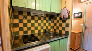 Eine kompakte Küche mit grünen Schränken, einer karierten Spritzschutzwand, einem Edelstahl-Spülbecken und einem kleinen Kühlschrank.