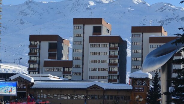 Ein Hotel mit mehreren Etagen, einem Schild für Skipässe und verschneiten Bergen im Hintergrund.