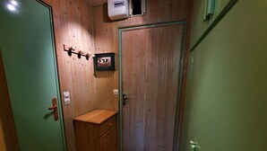 Ein kleiner Raum mit Holzwänden und einer grünen Tür. Ein Holzschrank und ein gerahmtes Bild sind an der Wand zu sehen.