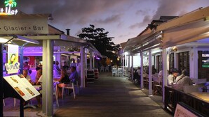 An outdoor bar area with tables and chairs, a menu stand, and a neon sign. - Duplex apartment located opposite the Golf de Saint-François.  (Saint-François)