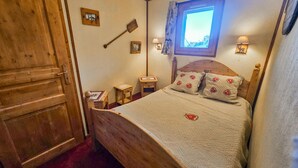 Een gezellige slaapkamer met een houten bed, een klein nachtkastje, een nachtkastje, een houten garderobe en een raam met uitzicht.