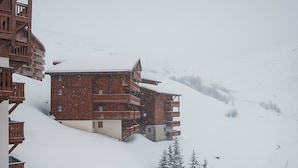 Een meerlaags gebouw met balkons, omringd door met sneeuw bedekte bomen en een besneeuwd landschap.