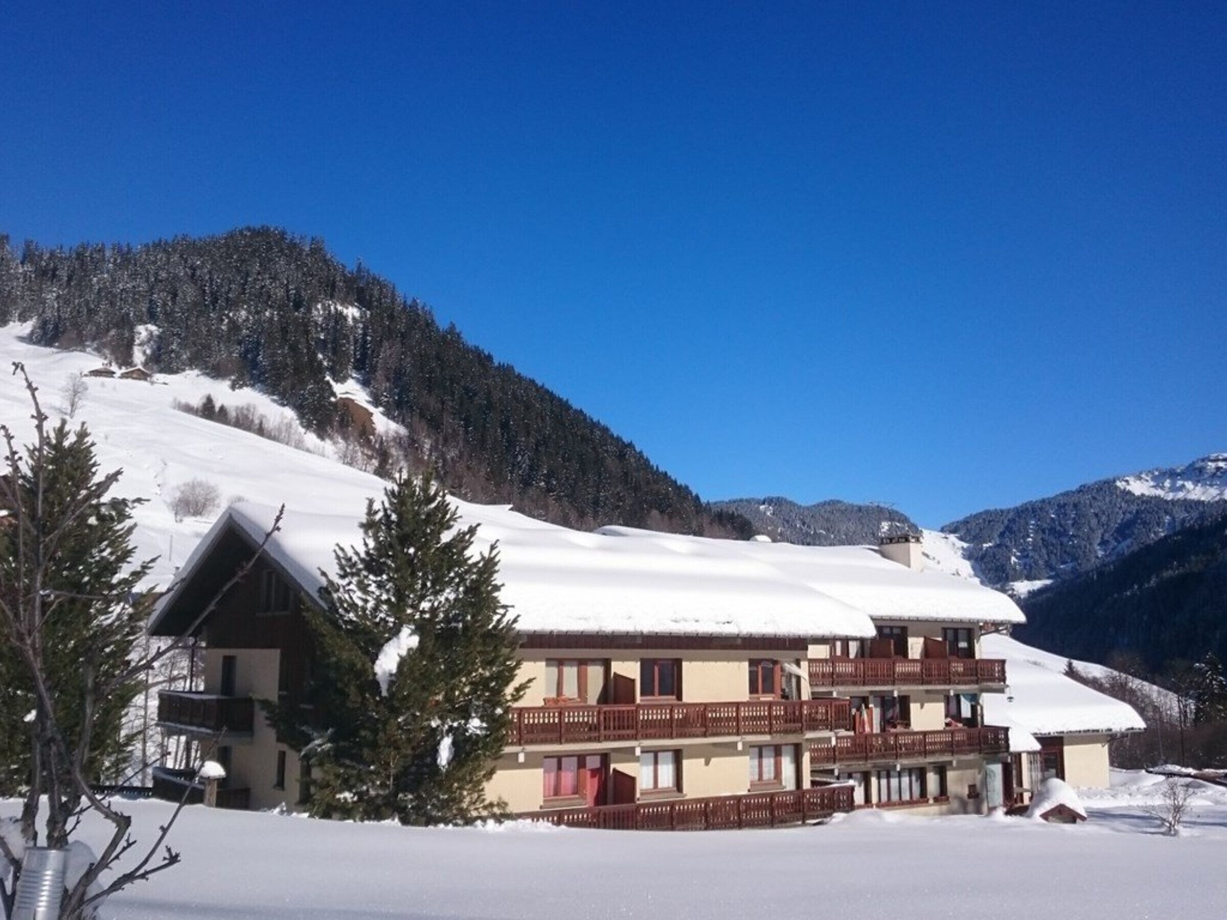 Ein mehrstöckiges Gebäude mit Balkonen, umgeben von schneebedeckten Bergen und Bäumen.