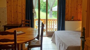 A room with a wooden interior, a dining table with chairs, a bed, a window with curtains, and a view of greenery outside. - Quiet apartment for 4, at the foot of the slopes with parking (Arêches-Beaufort)