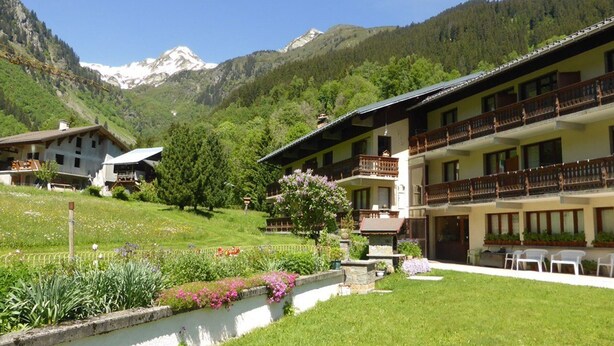 A hotel with a mountain backdrop, featuring a well-maintained garden, outdoor seating, and a traditional architectural style. - Quiet apartment for 4, at the foot of the slopes with parking (Arêches-Beaufort)
