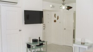 A modern hotel room with a flat-screen TV mounted on the wall, a glass coffee table, a bed, and a small bedside table with a lamp. - Luxurious beach  front self-catering apartment in the heart of Ocho Rios Jamaica (Ocho Rios)