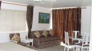 A room with a bed, a sofa, a dining table with chairs, a ceiling fan, and curtains. - Luxurious beach  front self-catering apartment in the heart of Ocho Rios Jamaica (Ocho Rios)